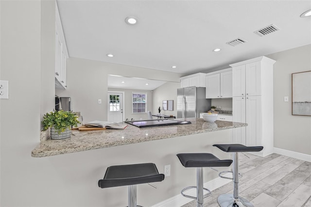 812 60th St S, Gulfport, FL 33707 - kitchen featuring freestanding refrigerator, a peninsula, white cabinets, a kitchen bar, and light stone counters