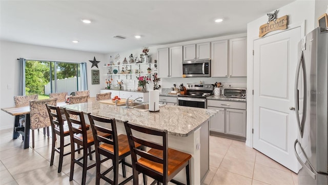 3739 Capri Coast Dr, Plant City, FL 33565 - kitchen with stainless steel appliances, gray cabinets, light tile patterned floors, a kitchen bar, and a center island with sink