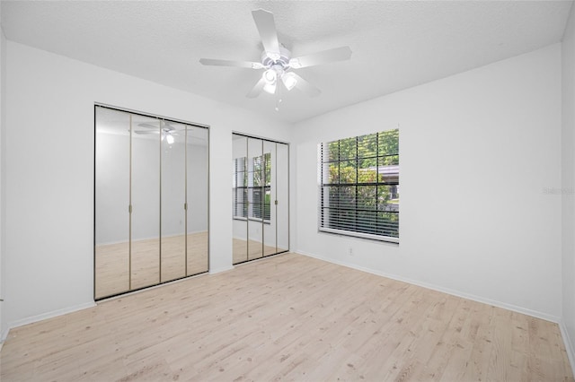 3447 Killdeer Pl, Palm Harbor, FL 34685 - unfurnished bedroom featuring multiple closets, wood finished floors, baseboards, a ceiling fan, and a textured ceiling