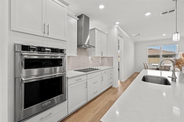 9271 Rally Spring Loop, Wesley Chapel, FL 33545 - kitchen featuring double oven, a sink, wall chimney exhaust hood, light wood-style floors, and tasteful backsplash