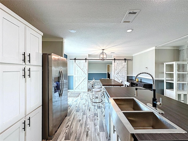 8851 C 469, Center Hill, FL 33514 - kitchen featuring stainless steel fridge with ice dispenser, a barn door, a textured ceiling, white cabinets, and hanging light fixtures