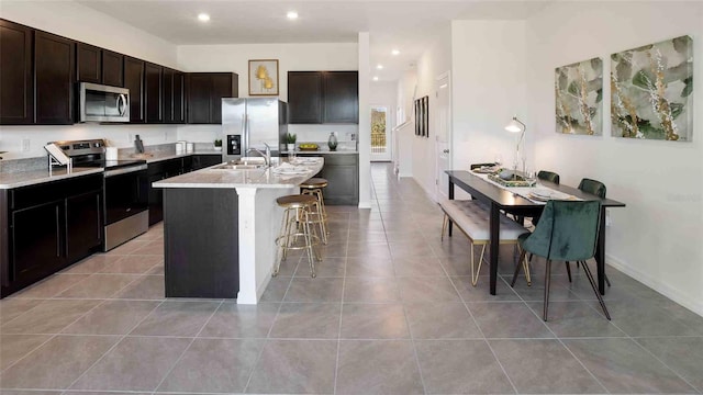 5112 Captain Davis Dr, Wimauma, FL 33598 - kitchen with appliances with stainless steel finishes, a kitchen breakfast bar, a center island with sink, a sink, and light tile patterned floors