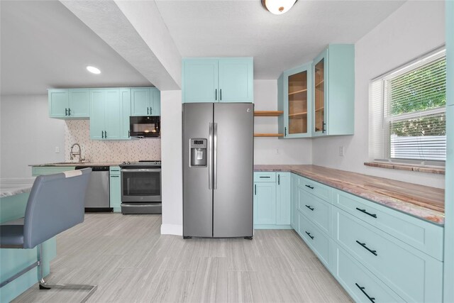 11363 Cocoa Beach Dr, Riverview, FL 33569 - kitchen featuring stainless steel appliances, glass insert cabinets, blue cabinets, tasteful backsplash, and light countertops