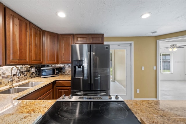 8918 Carmen Ln, Port Richey, FL 34668 - kitchen featuring stainless steel appliances, a sink, backsplash, brown cabinets, and light stone counters