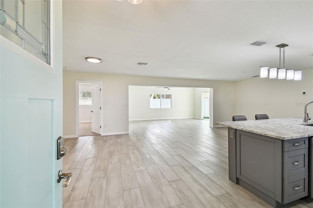 94 Nicholas Dr, Dunedin, FL 34698 - kitchen featuring gray cabinetry, light wood-type flooring, baseboards, hanging light fixtures, and light stone counters