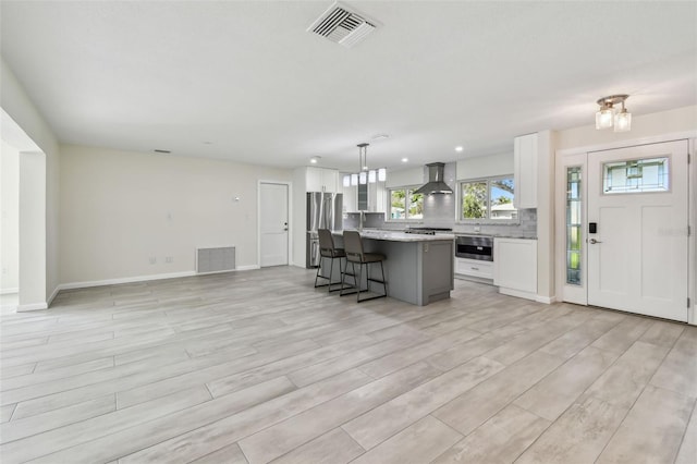 94 Nicholas Dr, Dunedin, FL 34698 - kitchen with wall chimney range hood, appliances with stainless steel finishes, white cabinets, a kitchen breakfast bar, and a center island