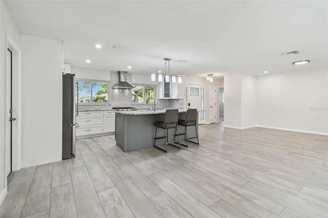 94 Nicholas Dr, Dunedin, FL 34698 - kitchen featuring wall chimney exhaust hood, freestanding refrigerator, light wood finished floors, a center island with sink, and white cabinets