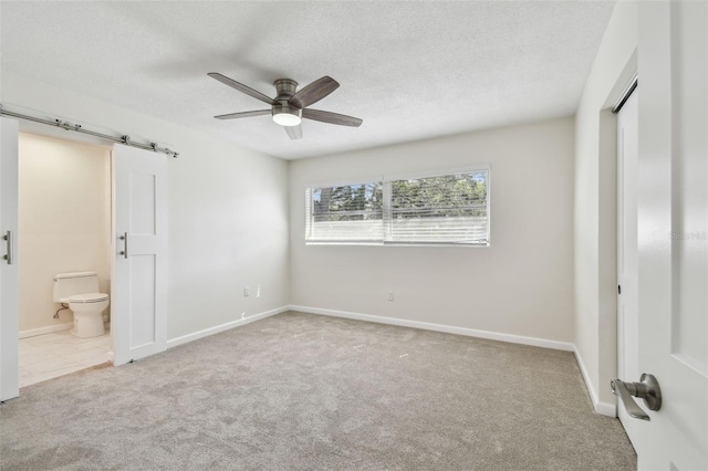 94 Nicholas Dr, Dunedin, FL 34698 - unfurnished bedroom featuring carpet floors, a barn door, a textured ceiling, connected bathroom, and ceiling fan
