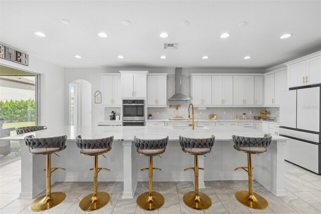 33255 Kateland Dr, Wesley Chapel, FL 33545 - kitchen featuring freestanding refrigerator, wall chimney range hood, arched walkways, decorative backsplash, and recessed lighting
