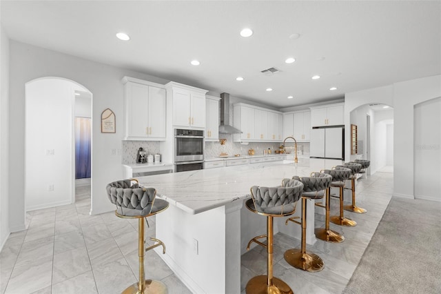 33255 Kateland Dr, Wesley Chapel, FL 33545 - kitchen featuring wall chimney range hood, arched walkways, recessed lighting, freestanding refrigerator, and white cabinetry