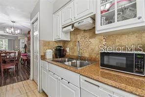 7523 Pitch Pine Cir Unit 184, Tampa, FL 33617 - kitchen with a sink, a chandelier, white cabinets, decorative backsplash, and glass insert cabinets