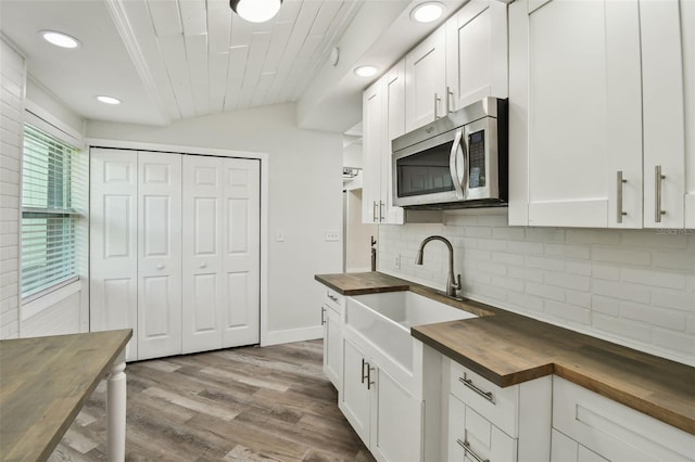 816 9th Ave SW, Largo, FL 33770 - kitchen featuring butcher block countertops, stainless steel microwave, a sink, backsplash, and white cabinets