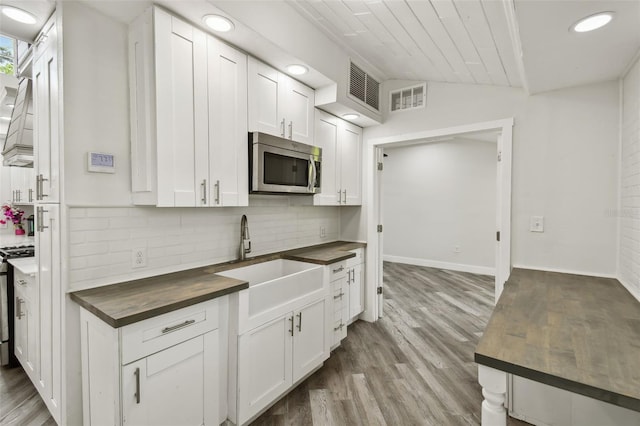816 9th Ave SW, Largo, FL 33770 - kitchen with butcher block counters, stainless steel microwave, a sink, decorative backsplash, and white cabinetry