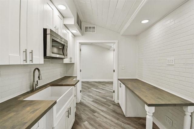 816 9th Ave SW, Largo, FL 33770 - kitchen with butcher block counters, stainless steel microwave, decorative backsplash, white cabinets, and brick wall
