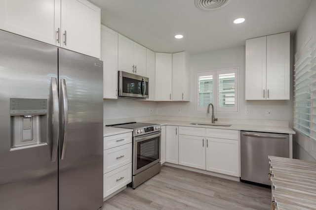 2271 Carolyn Dr, Dunedin, FL 34698 - kitchen with appliances with stainless steel finishes, a sink, light countertops, white cabinetry, and light wood-type flooring