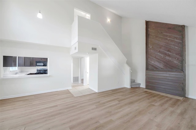 8521 N 29th St, Tampa, FL 33604 - unfurnished living room with a towering ceiling, light wood-style flooring, stairs, and baseboards