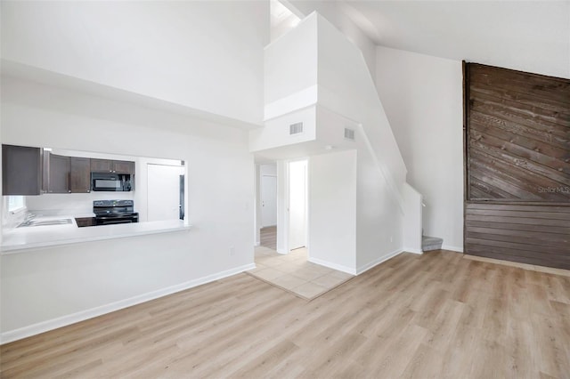 8521 N 29th St, Tampa, FL 33604 - unfurnished living room featuring a towering ceiling, light wood-style flooring, and baseboards