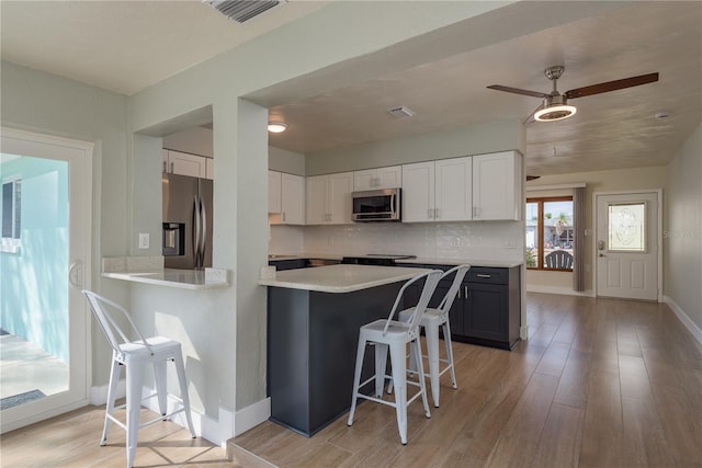 2010 Bayview Pl, Indian Rocks Beach, FL 33785 - kitchen with stainless steel appliances, a kitchen bar, light countertops, light wood-style floors, and white cabinetry