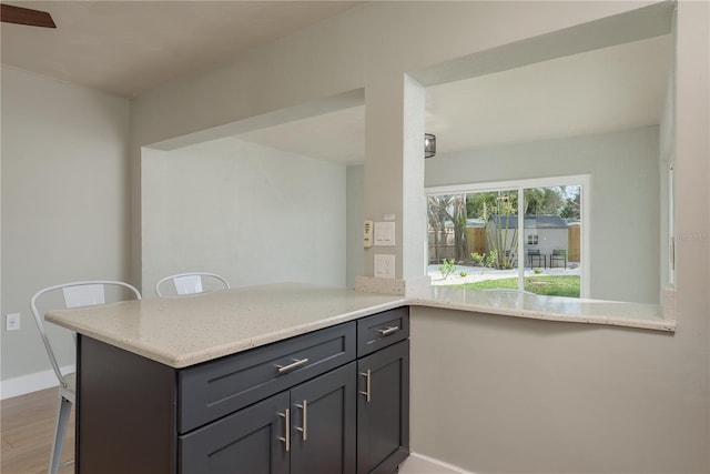 2010 Bayview Pl, Indian Rocks Beach, FL 33785 - kitchen featuring wood finished floors, a breakfast bar area, light stone counters, baseboards, and a peninsula