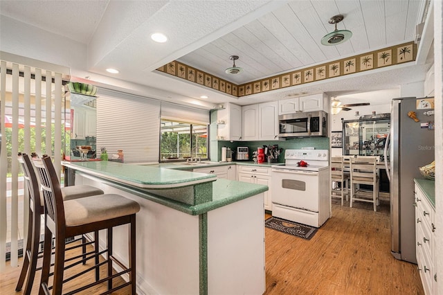 7700 Willow Brook Ct, Hudson, FL 34667 - kitchen with stainless steel appliances, white cabinetry, a peninsula, light wood-style floors, and a breakfast bar