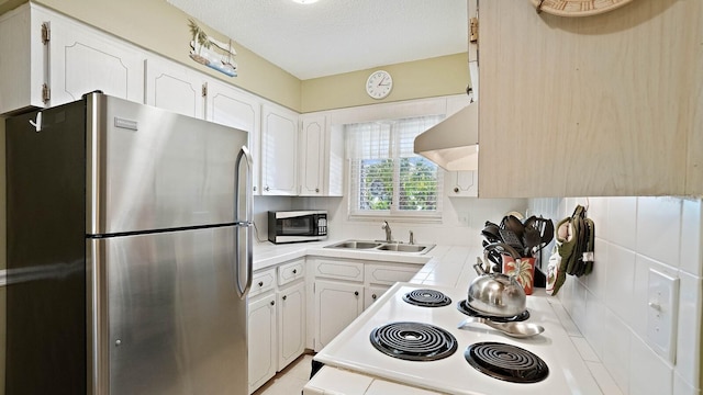 600 71st Ave Unit 16, St Pete Beach, FL 33706 - kitchen featuring freestanding refrigerator, a sink, stove, wall chimney exhaust hood, and white cabinetry