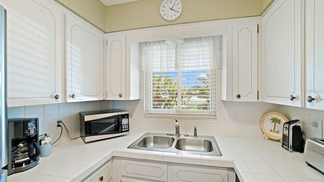 600 71st Ave Unit 16, St Pete Beach, FL 33706 - kitchen with black microwave, a sink, tile counters, and white cabinetry