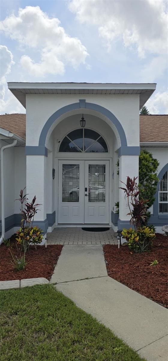 4500 Onorio St, New Port Richey, FL 34653 - view of exterior entry featuring french doors, a shingled roof, and stucco siding