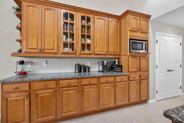 111 Falling Water Dr, Brandon, FL 33511 - kitchen featuring stainless steel microwave, dark stone counters, tasteful backsplash, glass insert cabinets, and light tile patterned floors