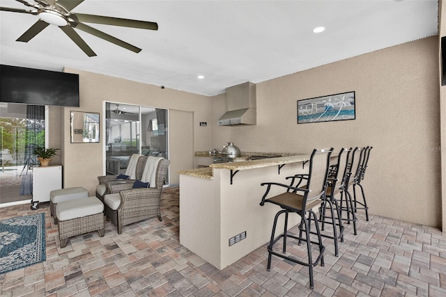 111 Falling Water Dr, Brandon, FL 33511 - kitchen with wall chimney exhaust hood, ceiling fan, a breakfast bar area, a peninsula, and light stone countertops