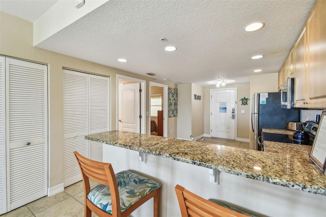 11605 Gulf Blvd Unit 506, Saint Petersburg, FL 33706 - kitchen featuring black / electric stove, light tile patterned floors, stainless steel microwave, light stone counters, and a textured ceiling