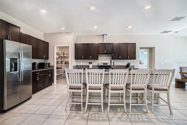 146 Rain Berry Ave, Ruskin, FL 33570 - kitchen with appliances with stainless steel finishes, dark brown cabinets, light tile patterned floors, a breakfast bar area, and an island with sink