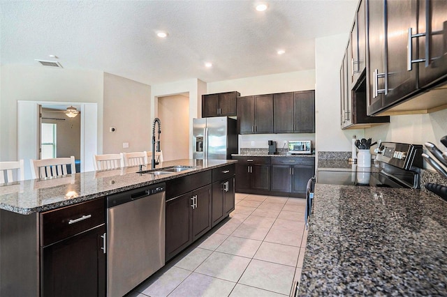146 Rain Berry Ave, Ruskin, FL 33570 - kitchen with appliances with stainless steel finishes, a kitchen island with sink, light tile patterned floors, dark brown cabinetry, and a textured ceiling