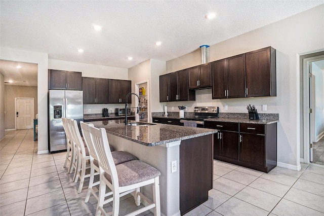 146 Rain Berry Ave, Ruskin, FL 33570 - kitchen with appliances with stainless steel finishes, light tile patterned floors, a kitchen breakfast bar, dark brown cabinetry, and a kitchen island with sink