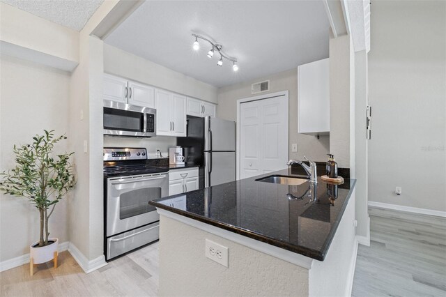 3301 Haviland Ct Unit 203, Palm Harbor, FL 34684 - kitchen featuring appliances with stainless steel finishes, light wood finished floors, a sink, white cabinets, and a peninsula