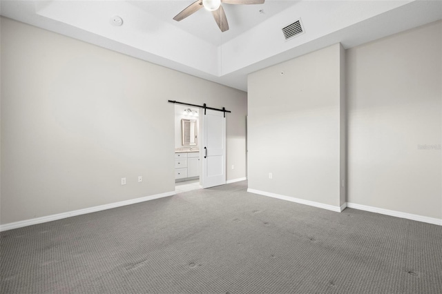 807 Callista Cay Loop, Tarpon Springs, FL 34689 - unfurnished bedroom featuring carpet, a barn door, a tray ceiling, baseboards, and connected bathroom