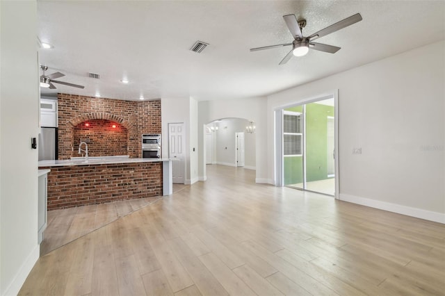9709 Bay Colony Dr, Riverview, FL 33578 - unfurnished living room featuring a ceiling fan, arched walkways, light wood-style floors, a sink, and baseboards