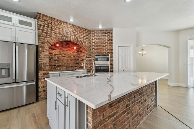 9709 Bay Colony Dr, Riverview, FL 33578 - kitchen with stainless steel appliances, a sink, brick wall, light wood-style floors, and light stone counters