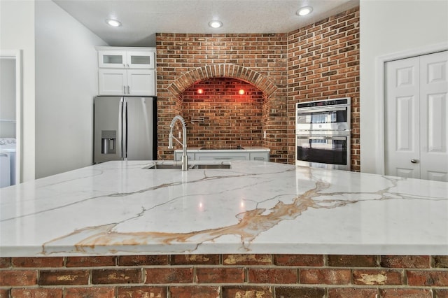 9709 Bay Colony Dr, Riverview, FL 33578 - kitchen featuring appliances with stainless steel finishes, light stone counters, brick wall, a sink, and glass insert cabinets