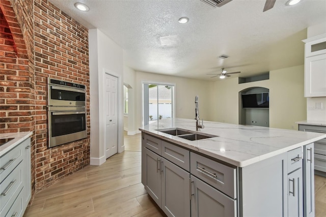 9709 Bay Colony Dr, Riverview, FL 33578 - kitchen featuring a sink, double oven, ceiling fan, gray cabinetry, and an island with sink