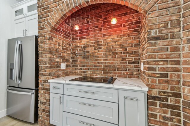 9709 Bay Colony Dr, Riverview, FL 33578 - kitchen with stainless steel refrigerator with ice dispenser, brick wall, light stone counters, black electric stovetop, and glass insert cabinets