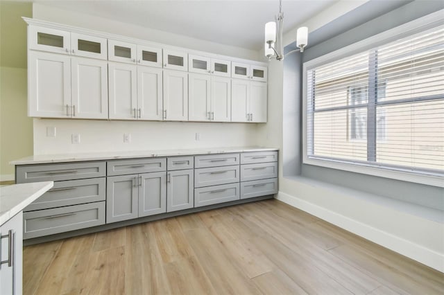 9709 Bay Colony Dr, Riverview, FL 33578 - kitchen featuring light wood-style floors, baseboards, hanging light fixtures, and glass insert cabinets