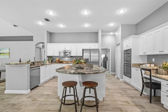 12009 Wandsworth Dr, Tampa, FL 33626 - kitchen featuring appliances with stainless steel finishes, light wood finished floors, a kitchen island, a peninsula, and dark stone countertops