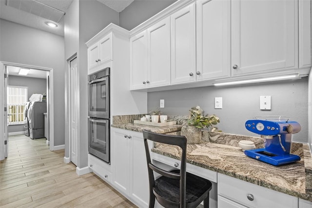 12009 Wandsworth Dr, Tampa, FL 33626 - kitchen featuring washer / dryer, stainless steel double oven, light stone counters, white cabinetry, and light wood-style floors