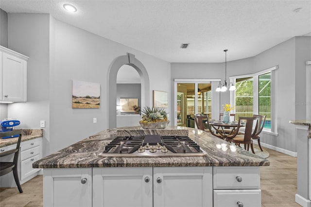 12009 Wandsworth Dr, Tampa, FL 33626 - kitchen with stainless steel gas cooktop, light wood-style flooring, white cabinets, a chandelier, and dark stone countertops