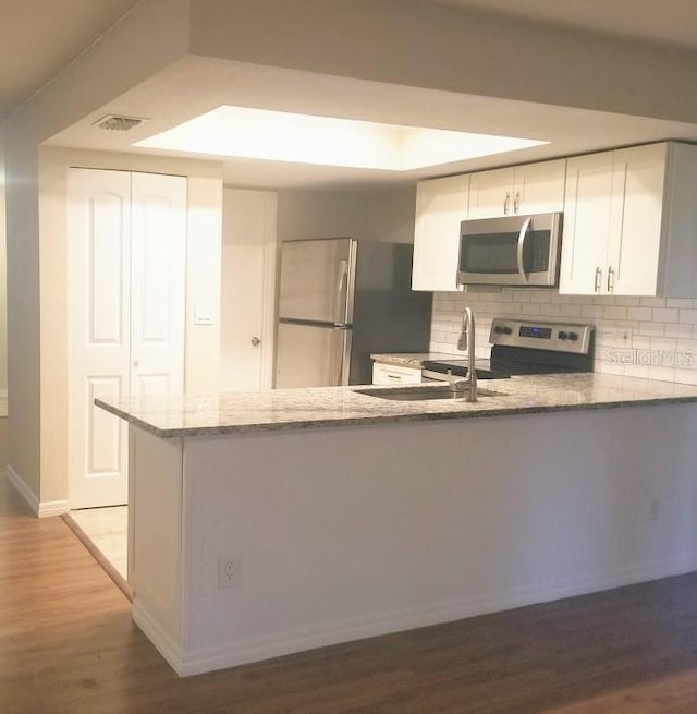 1841 Georgia Ave, Palm Harbor, FL 34683 - kitchen featuring stainless steel appliances, light stone countertops, a peninsula, light wood-type flooring, and white cabinets
