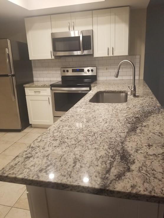 1841 Georgia Ave, Palm Harbor, FL 34683 - kitchen featuring stainless steel appliances, a sink, light stone countertops, and white cabinets