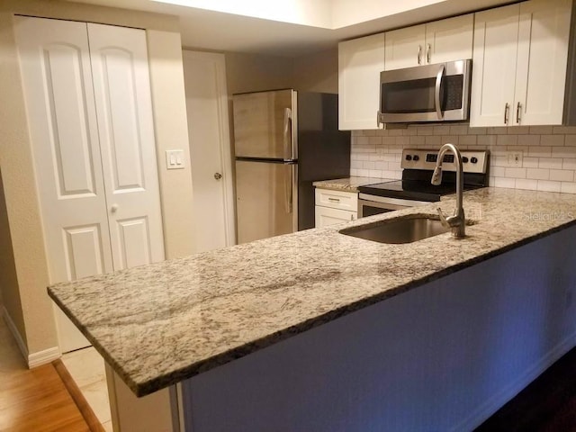 1841 Georgia Ave, Palm Harbor, FL 34683 - kitchen featuring appliances with stainless steel finishes, light stone counters, a sink, and white cabinetry