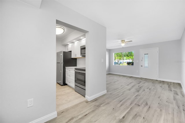 11224 82nd Ave Unit 104, Seminole, FL 33772 - kitchen with appliances with stainless steel finishes, ceiling fan, white cabinets, baseboards, and light wood-style flooring