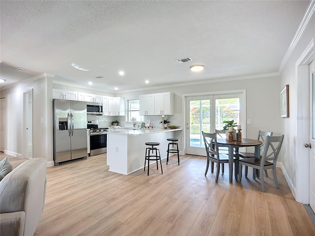 9929 Bay Dr, Gibsonton, FL 33534 - kitchen featuring stainless steel appliances, ornamental molding, a peninsula, light wood-style floors, and a breakfast bar