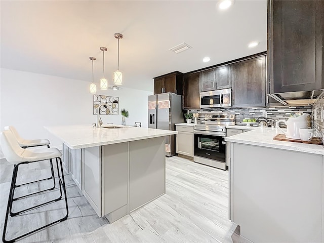 7125 S Shore Dr S, Saint Petersburg, FL 33707 - kitchen featuring stainless steel appliances, a sink, tasteful backsplash, dark brown cabinetry, and a center island with sink